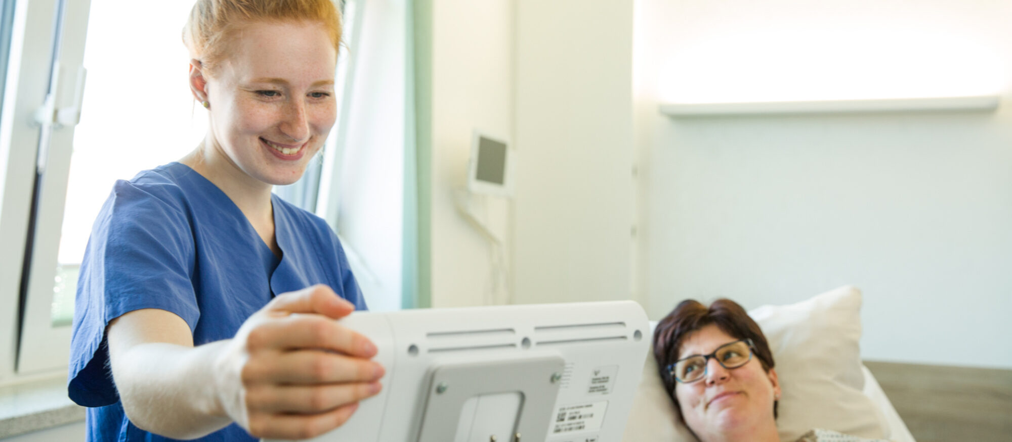 Azubi an der AK steht am PC bei Patientin